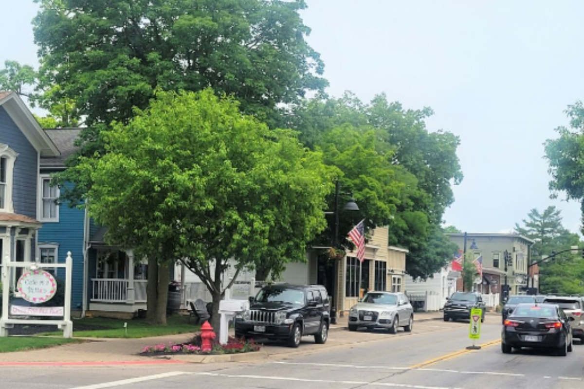 A street view of downtown Powell, Ohio, with local shops, American flags, and lush green trees.