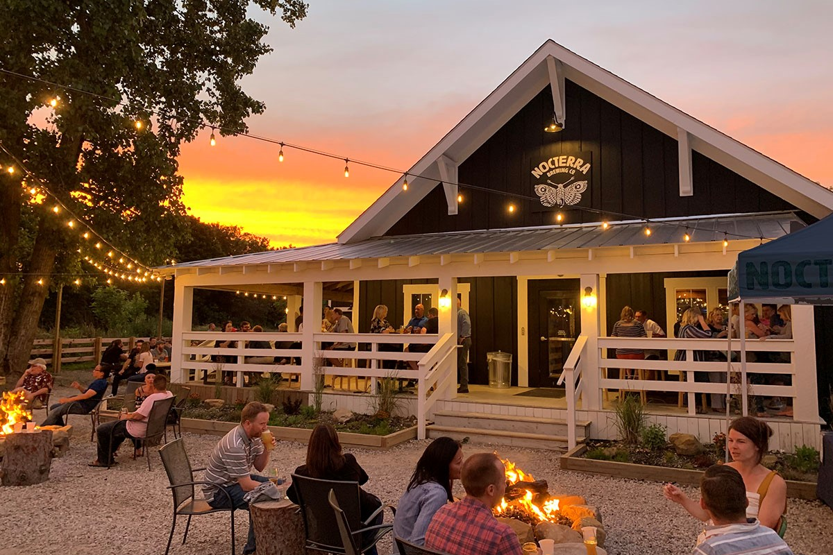 Outdoor patio of Nocterra Brewing Co. in Powell, Ohio at sunset with string lights and patrons around fire pits.