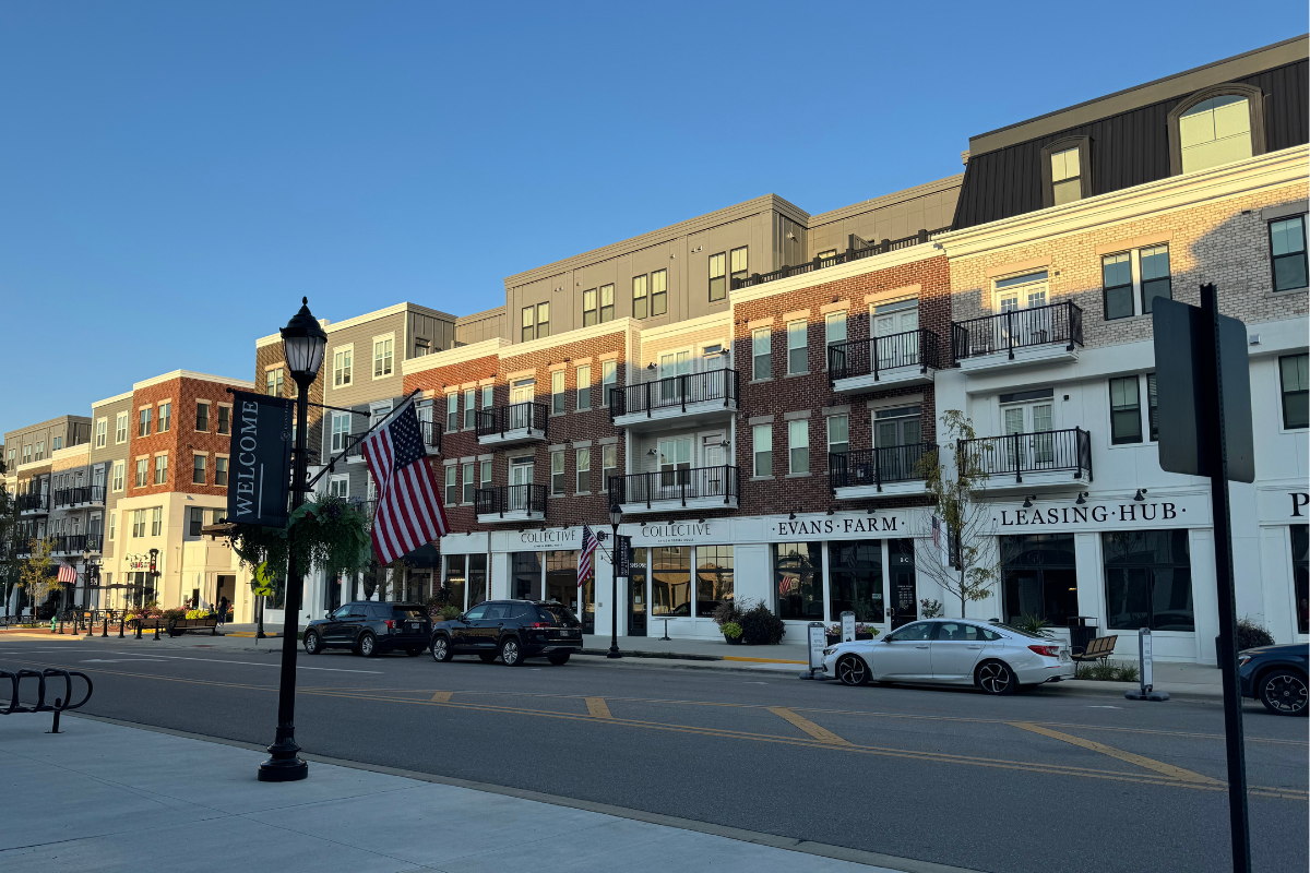 Street view of multi-story mixed-use buildings at Evans Farm during sunset with an American flag in the foreground.
