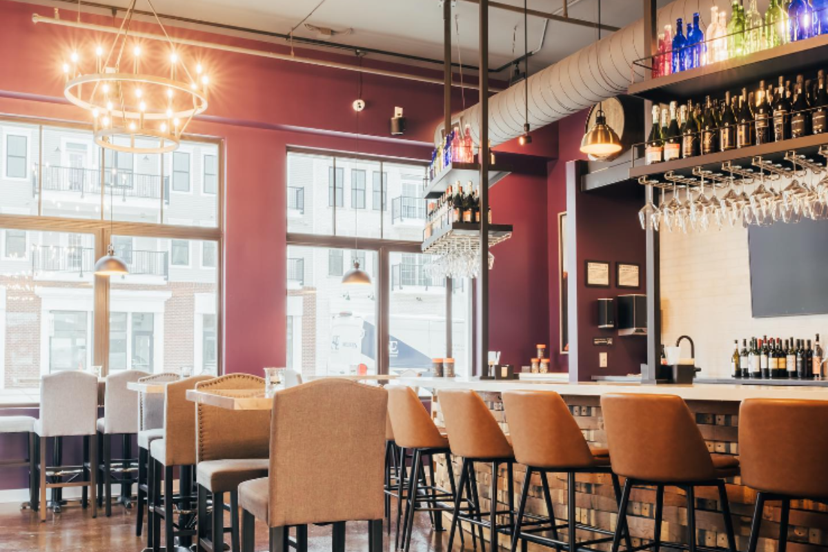 Modern interior of Prime and Vine wine bar featuring plum-colored walls, leather bar stools, and warm chandelier lighting.