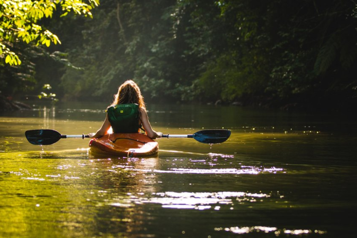 A person kayaking on the calm, sunlit waters of Big Walnut Creek surrounded by dense trees in Galena, OH.