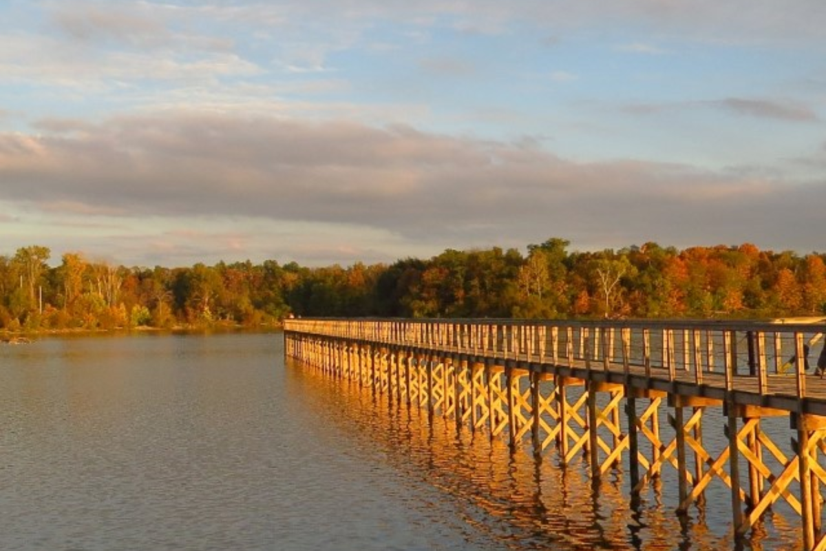 Long wooden boardwalk at Hoover Reservoir in Galena, Ohio, with golden hour sunlight and autumn trees in the background.