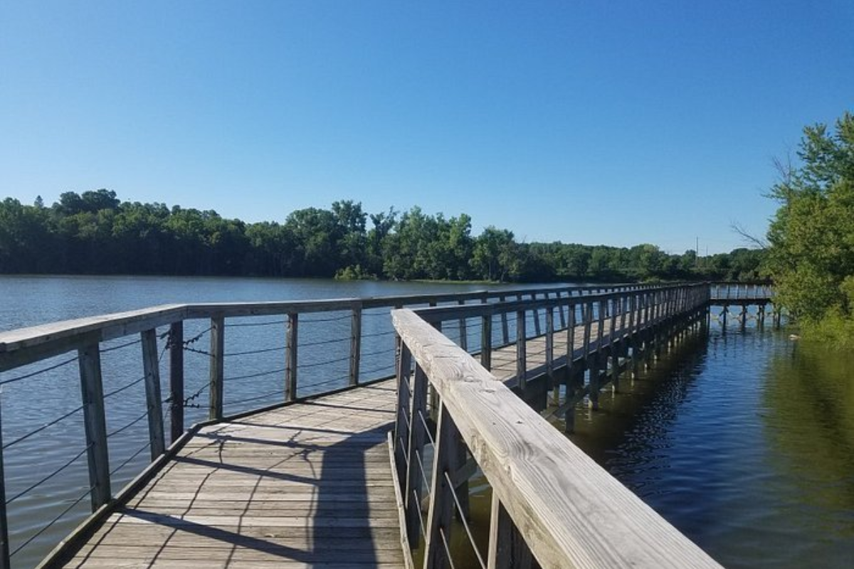 Scenic view of the wooden boardwalk at the Hoover Mudflats in Galena, Ohio, stretching over calm water under a blue sky.