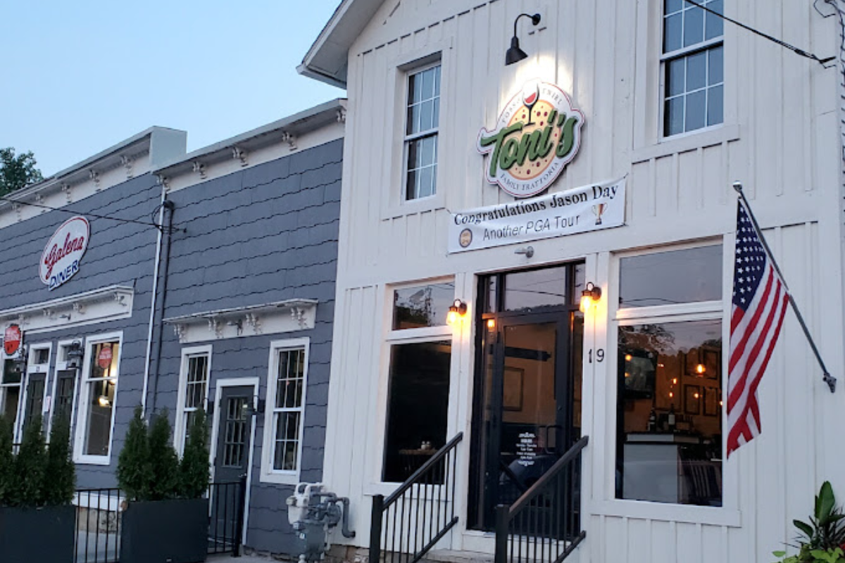 Exterior of Toni's Trattoria, a white wood-sided restaurant with an American flag out front.