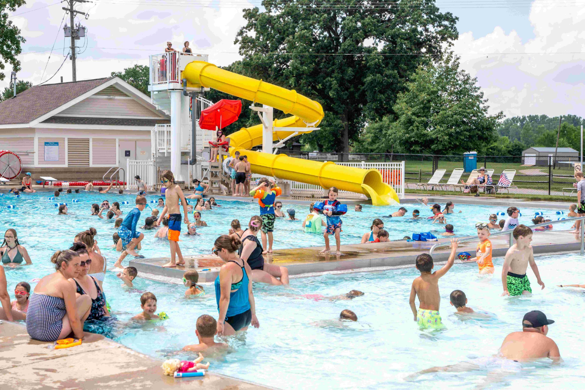 Families and children playing in the pool and using the yellow water slide at Plain City Aquatic Center.